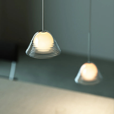 A modern pendant light with a ribbed, dome-shaped clear glass shade glowing warm white, suspended by a thin cord.