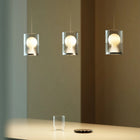 Three modern cylindrical pendant lights with ribbed shades and glowing round bulbs, hanging over a tabletop in a warm interior setting.